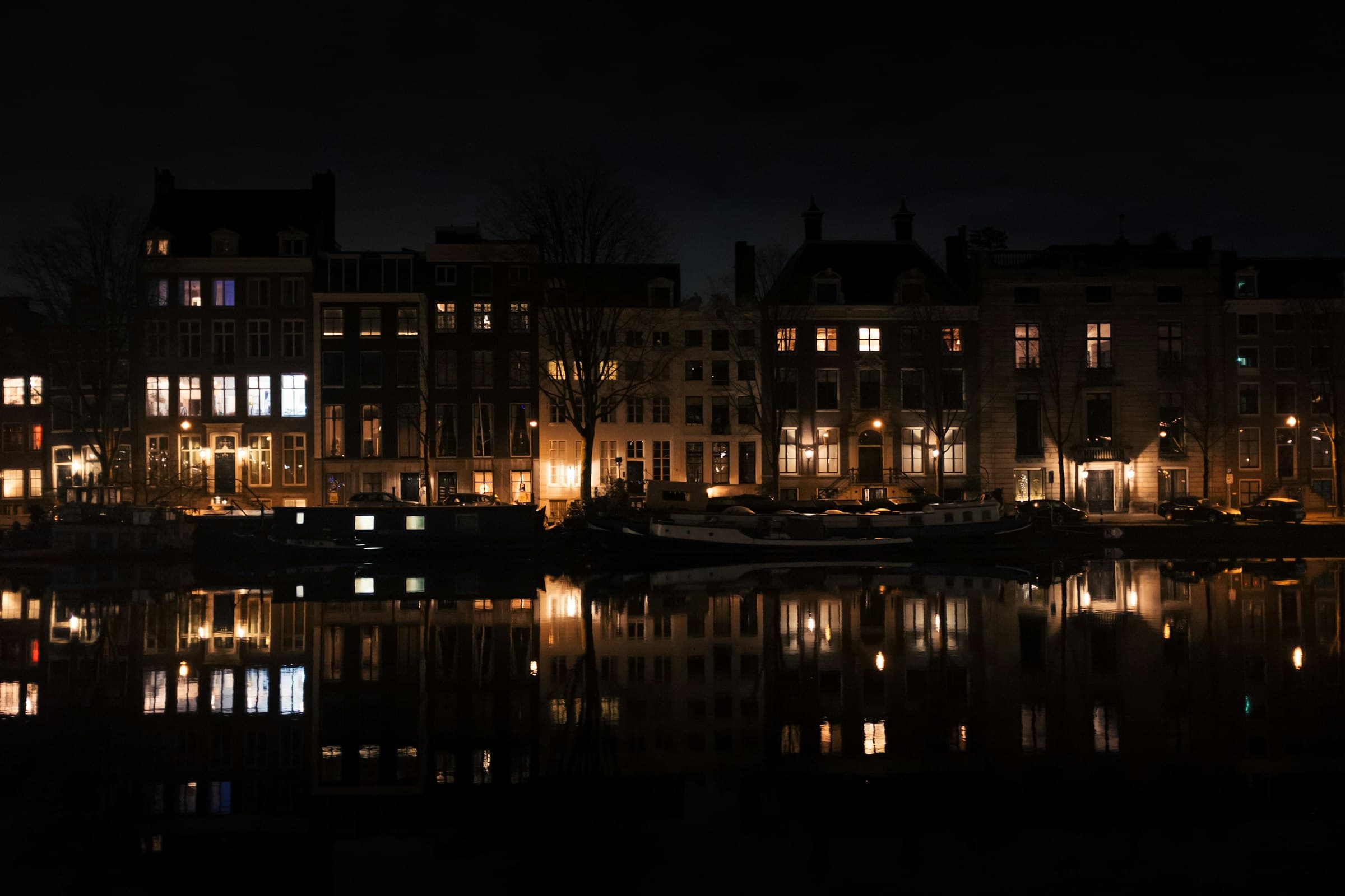 Grachtenpanden bij nacht met verlichte ramen die weerspiegelen in het water