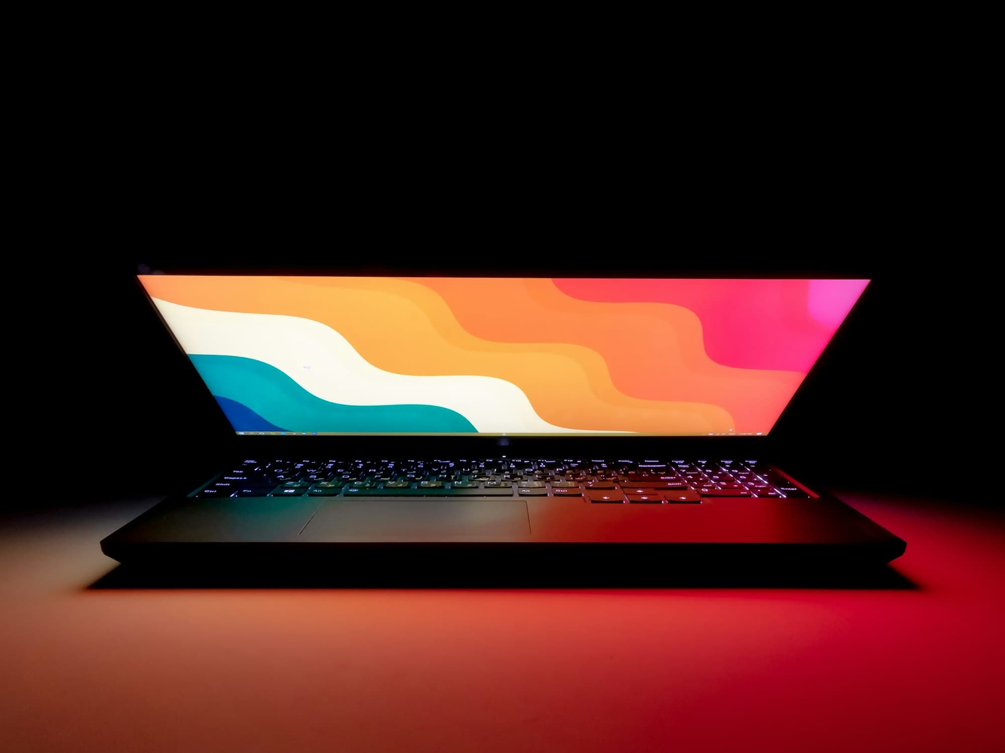 Een opengeklapte laptop met een kleurrijk scherm in een donkere kamer
