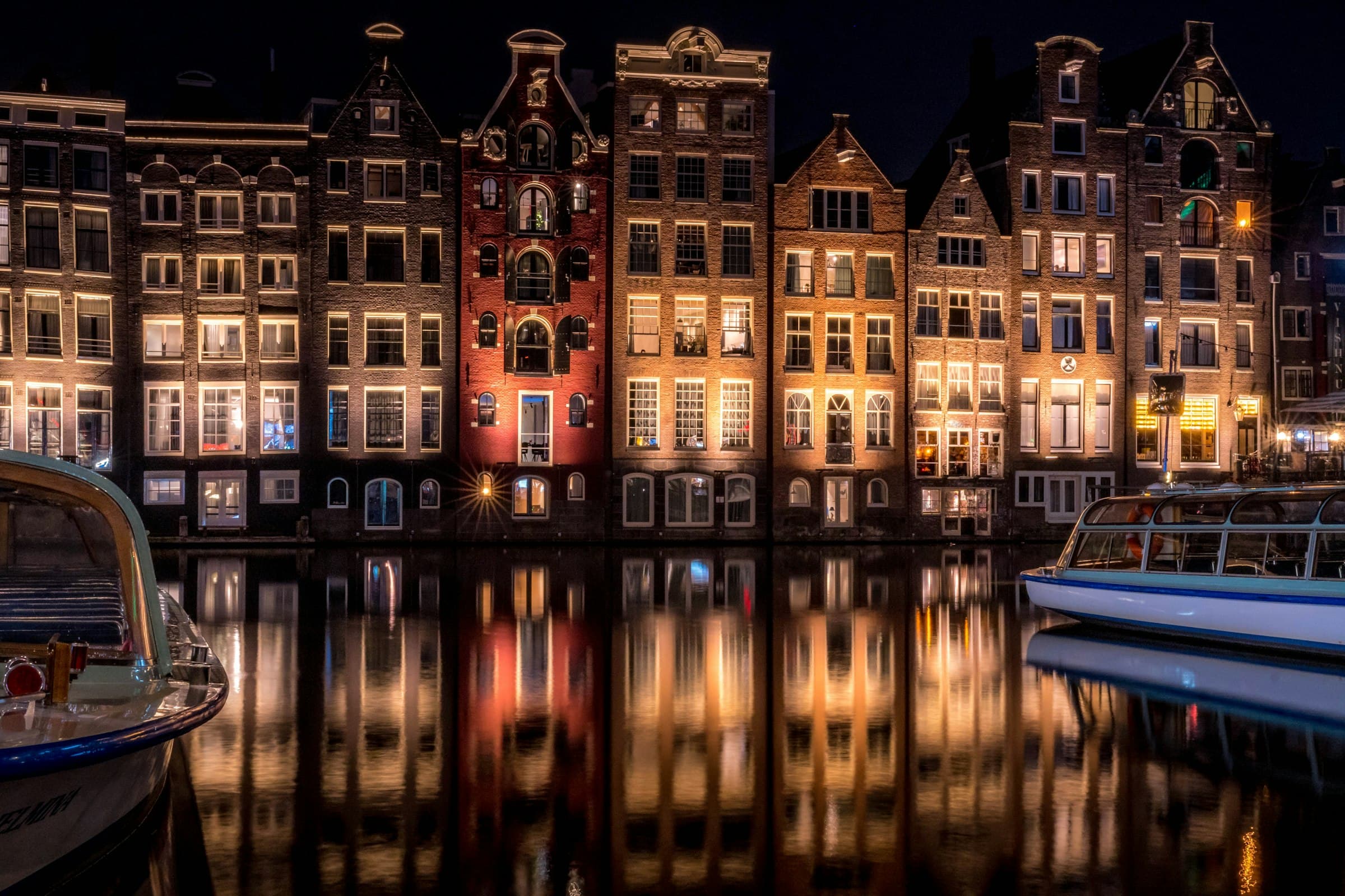 Grachtenpanden aan het Damrak in Amsterdam bij nacht, met verlichte ramen die weerspiegelen in het water