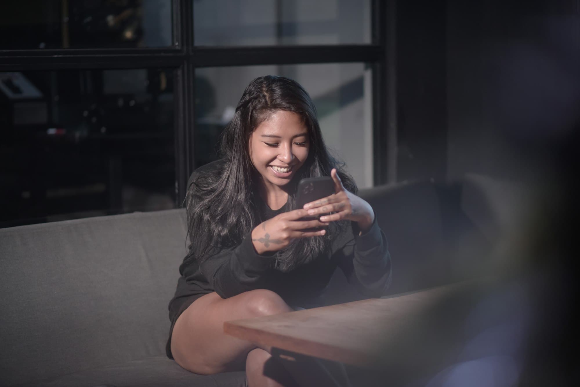 Een vrouw zit lachend op de bank met haar telefoon in haar handen