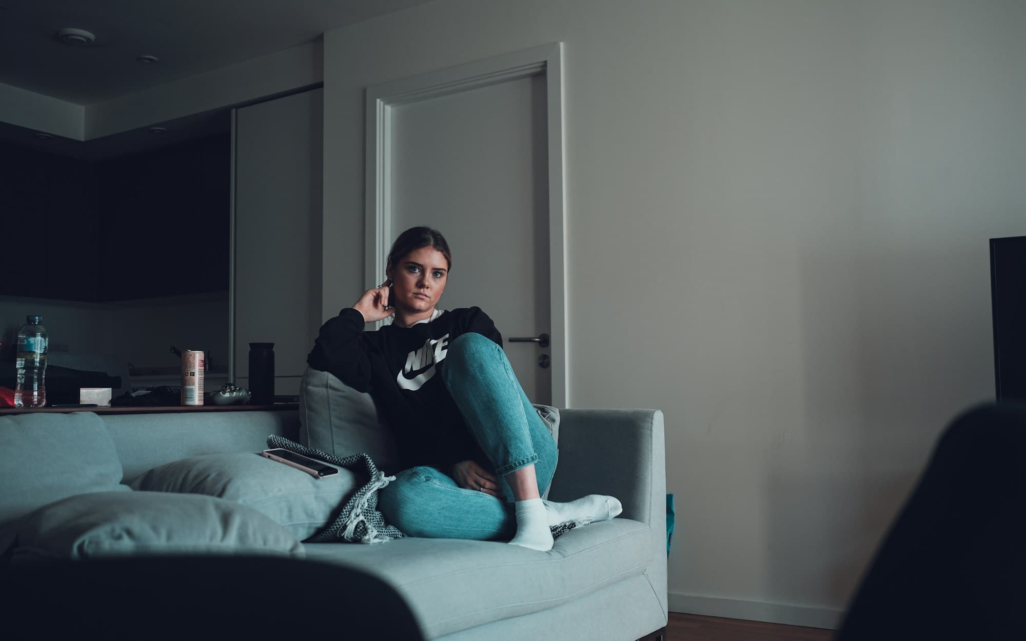 Een vrouw zit ontspannen op de bank en kijkt op haar telefoon