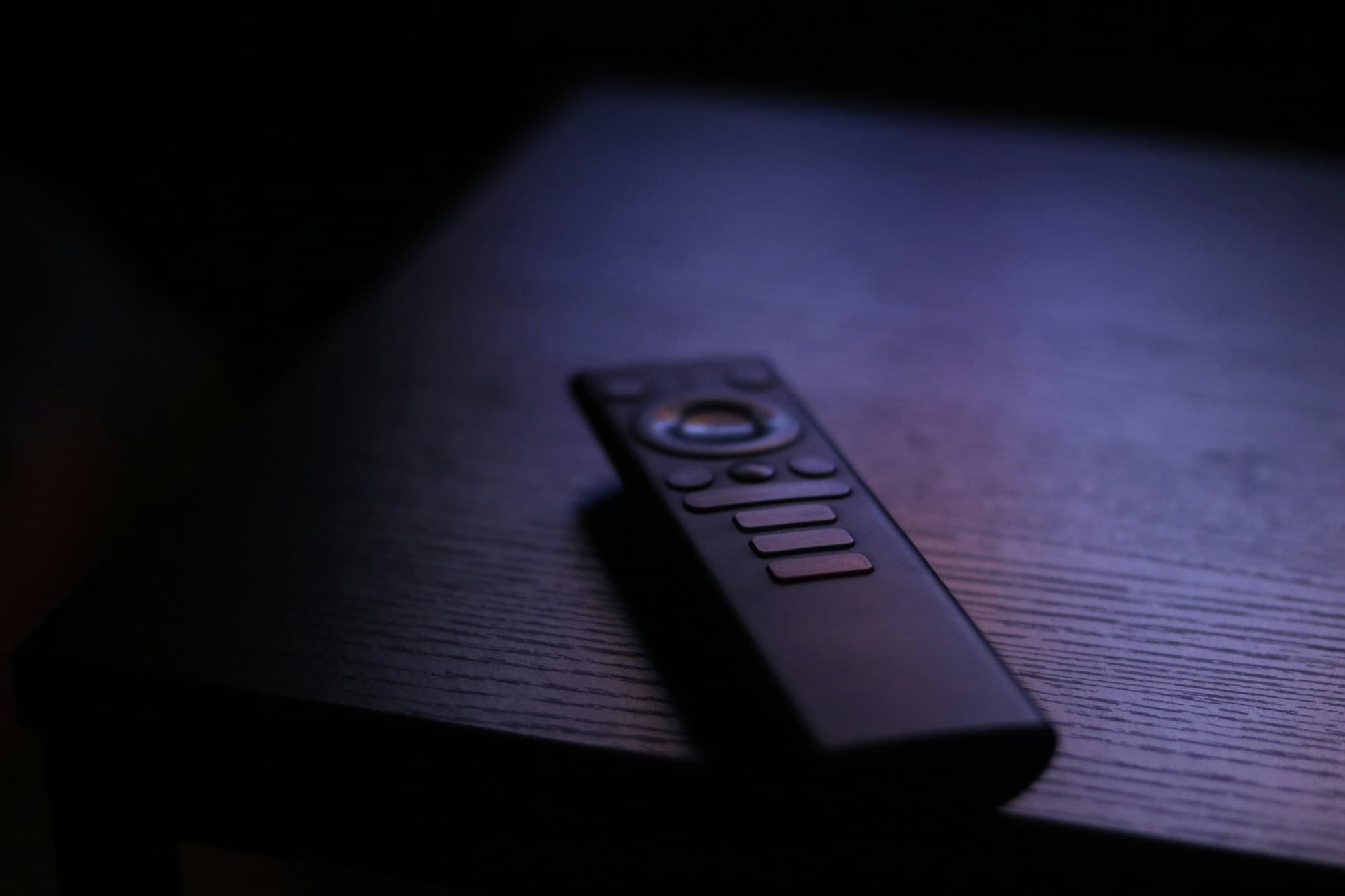 Een zwarte afstandsbediening op een donkere houten tafel, in een streep licht