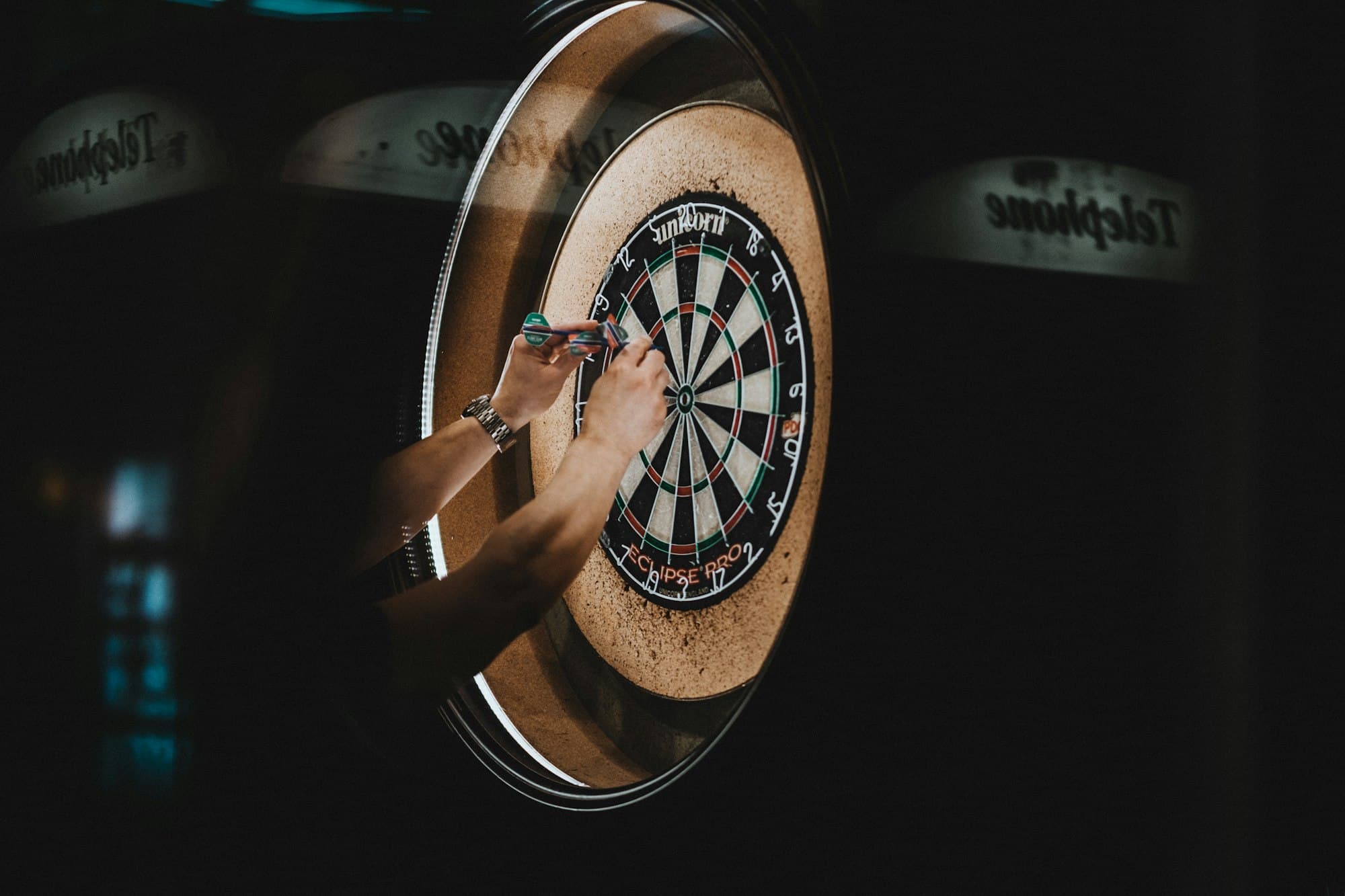Een hand trekt pijlen uit een dartbord in een donkere zaal