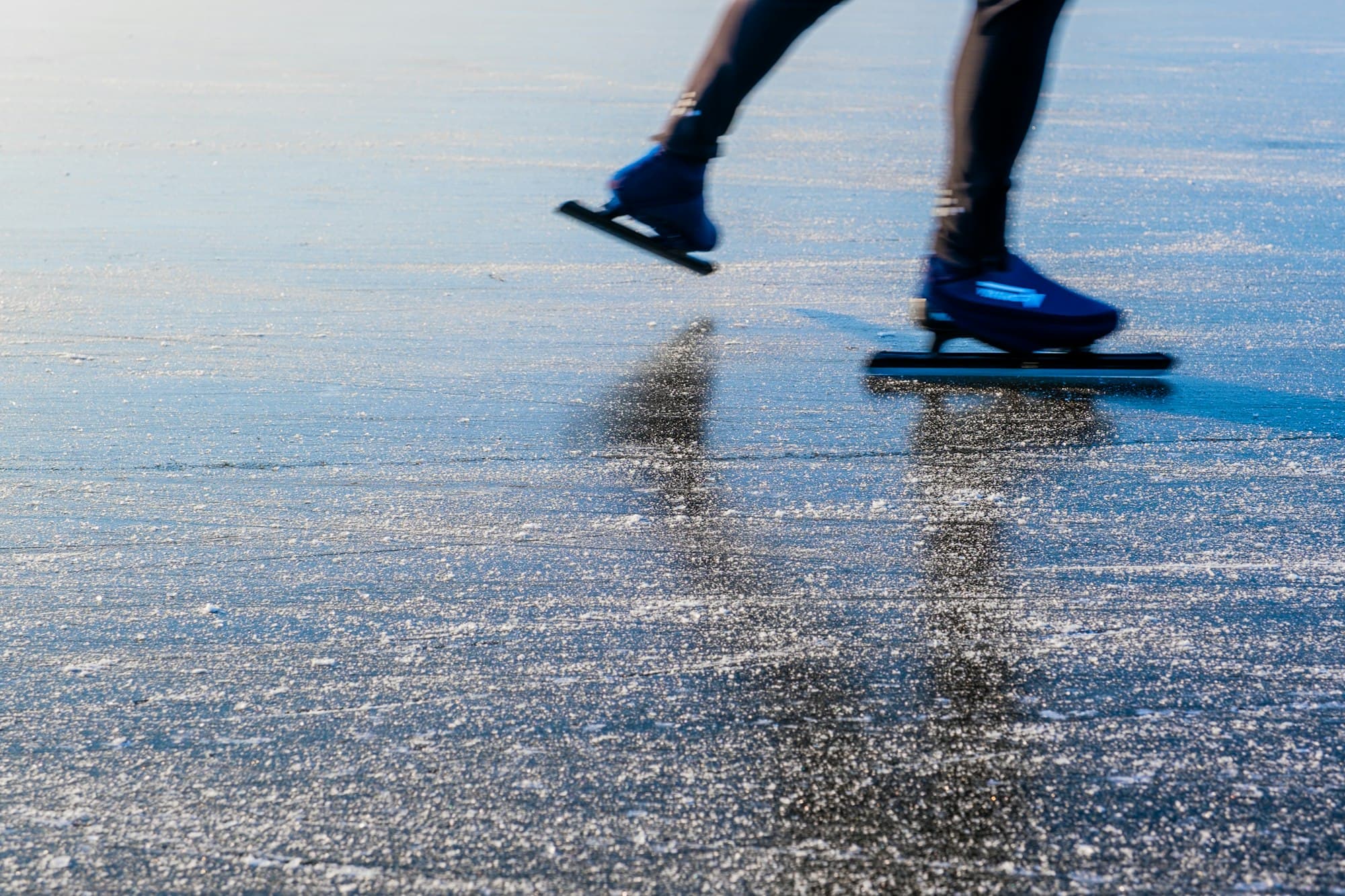 De benen van een schaatser op spiegelend ijs, in volle vaart