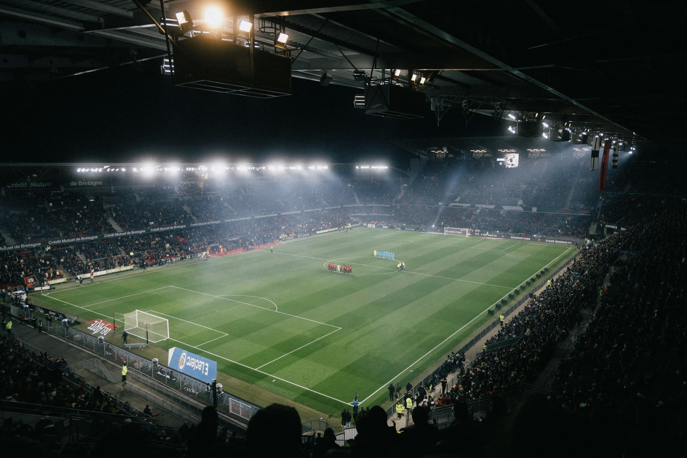 Voetbalstadion bij avond, het veld verlicht door schijnwerpers in de mist